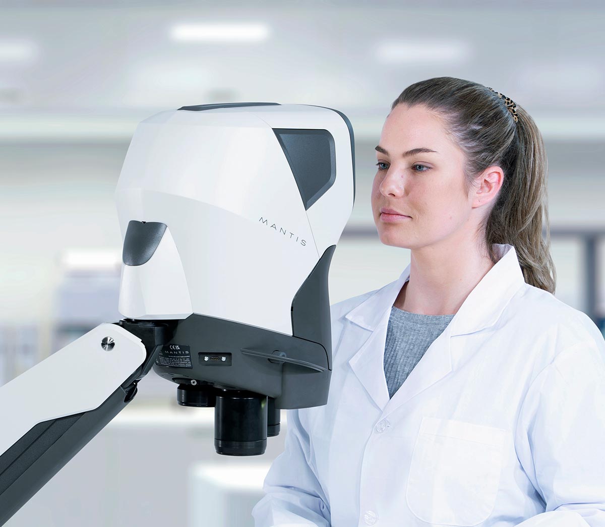 Dental technician in white coat looking into Mantis viewer 1200x1045px Dental technician in white coat looking into Mantis viewer