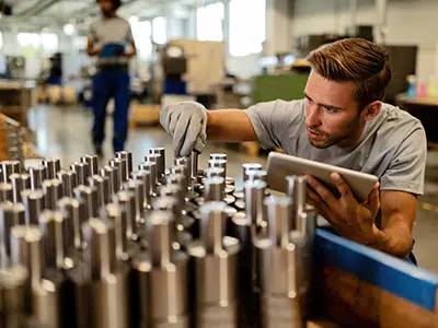iStock-1152648684-goodsin-400×300 Hombre inspeccionando piezas metálicas en una línea de producción
