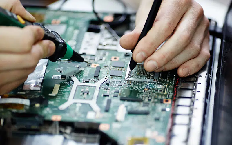 AURA-solder-PCB-AdobeStock_136939755-800×500 Primer plano de las manos de una persona utilizando un soldador en una placa de circuito impreso (PCB).